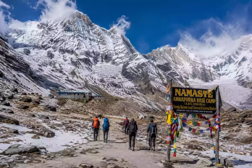 Trekkers at Annapurna Base Camp surrounded by towering snow-capped Annapurna peaks under clear alpine skies in Nepal.