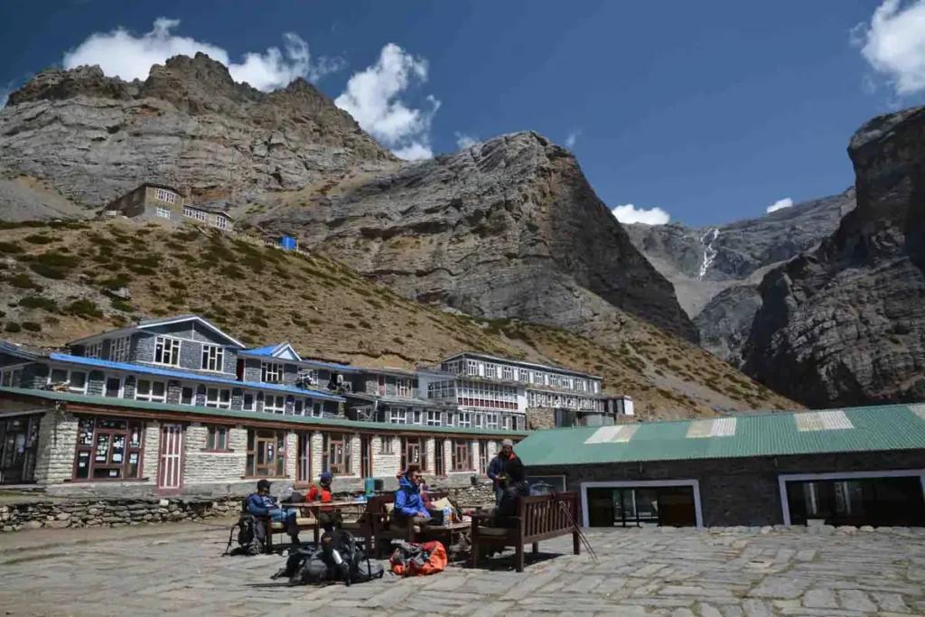Trekkers resting with backpacks outside a teahouse lodge beneath rocky Himalayan cliffs on the Annapurna Circuit